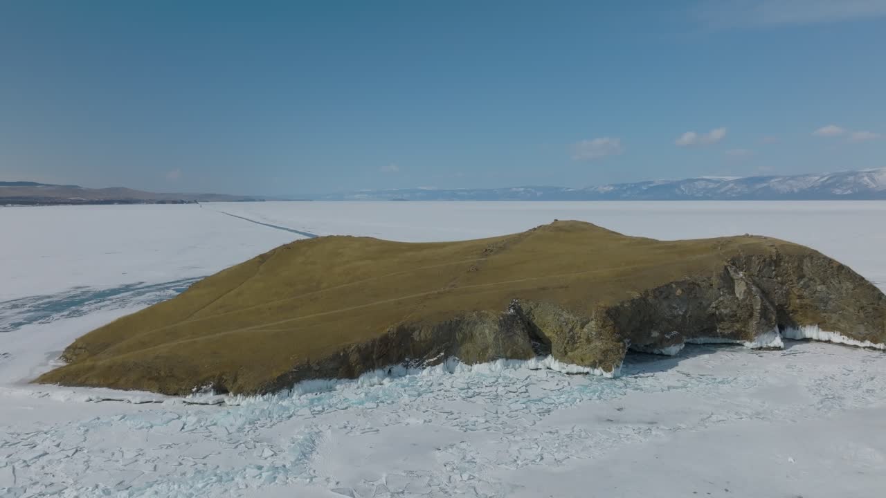 Droneoptagelse af Kap Kharantsy med klippefyldte klipper og græsklædt højderyg over revnet is på den frosne Bajkalsø, Olkhon-øen, Irkutsk oblast, Rusland