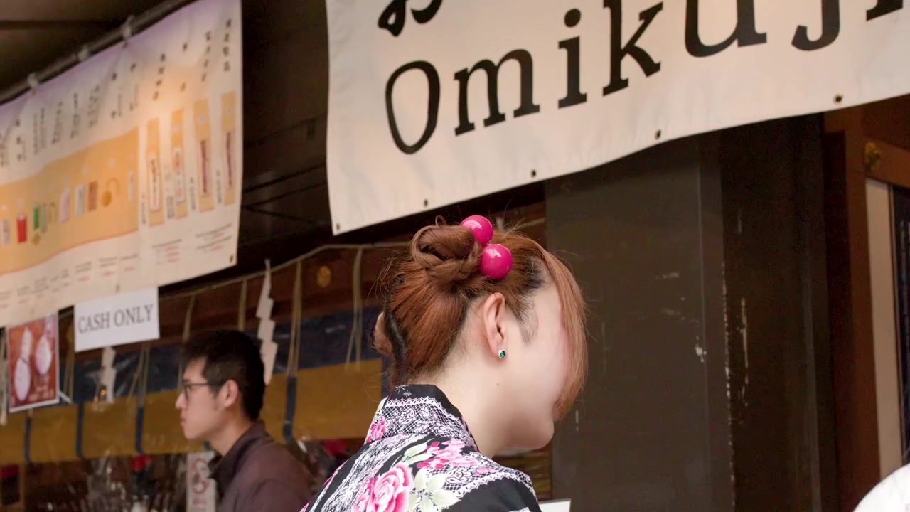 Una donna in yukata tradizionale sta davanti a una bancarella di Omikuji in un santuario giapponese.