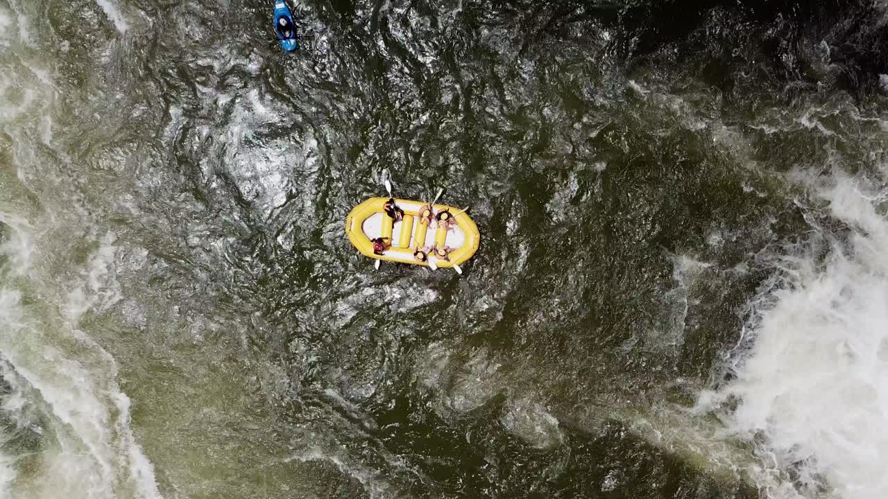 Drone zooming vertically away over a rafting boat and kayak between the waterfalls of the Nile River in Jinja, Uganda