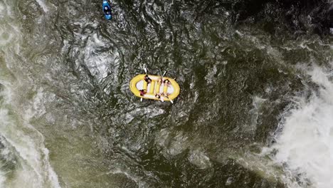 Drone-zooming-vertically-away-over-a-rafting-boat-and-kayak-between-the-waterfalls-of-the-Nile-River-in-Jinja,-Uganda