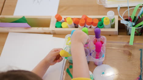 little child drip painting holding dropper and sucks in colored water into pipette from containers - hands close-up