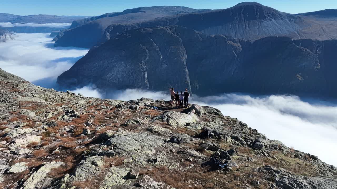Two couples stand on a cliff, drone circles with parallax, then ascends to reveal the steep Naeroyfjord drop