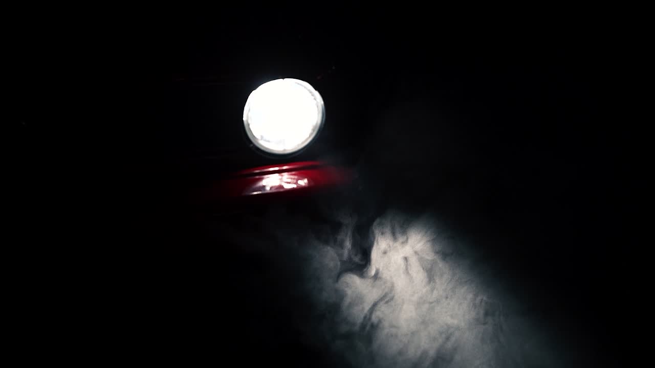 Fog or mist moving in light beam of red car round headlight, slow motion close up