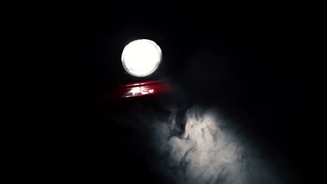 fog or mist moving in light beam of red car round headlight, slow motion close up