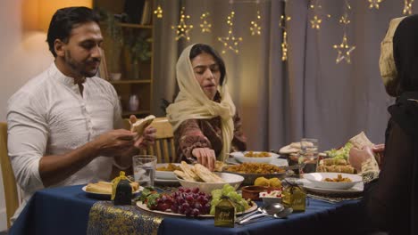 familia musulmana sentada alrededor de una mesa en casa comiendo para celebrar el eid