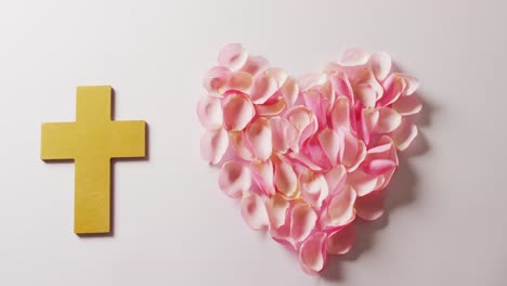 Video-of-yellow-christian-cross-and-heart-shape-of-pink-rose-petals-on-white-background