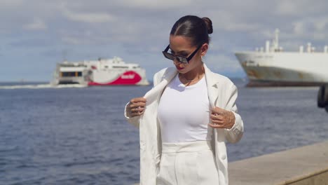 una mujer joven de pie en ropa de negocios en un paseo marítimo con un ferry pasando en el fondo