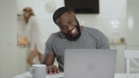 Laughing-black-man-sitting-at-open-kitchen.-Pretty-woman-standing-background