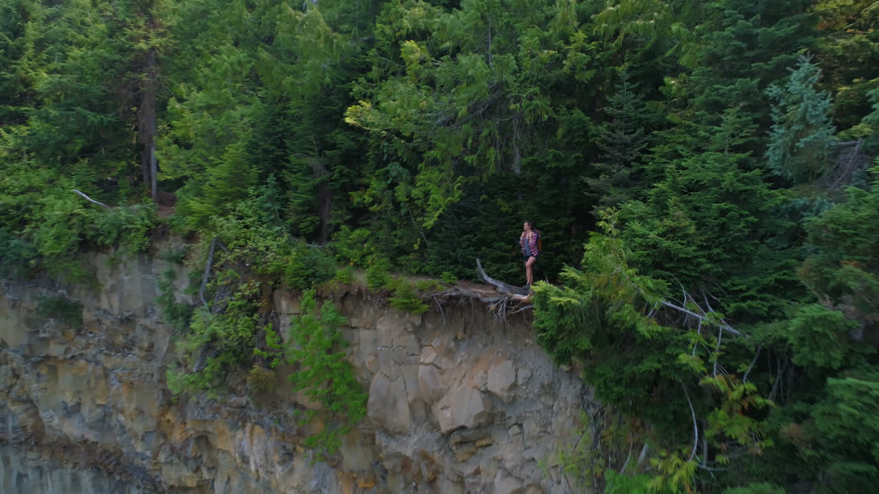 Female hiker standing on cliff in forest 4k