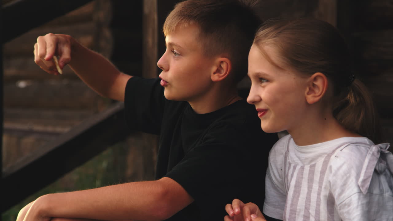 Siblings Eating Pancakes on Porch in Morning Happy Boy and Girl Laughing and Talking while Sitting Near Wooden House and Eating Fresh Pancakes in Sunny Morning in Countryside