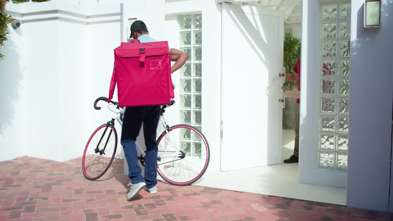 Mensajero afroamericano recibiendo una caja de pizza, cerrando la cremallera de la bolsa en el patio y montando en bicicleta para la entrega.