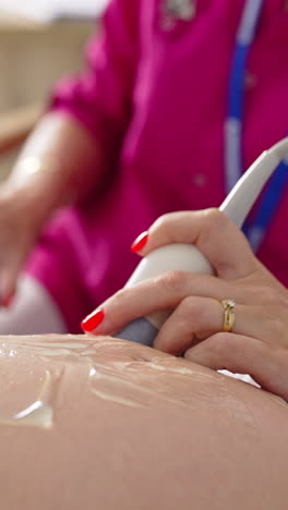 pregnant woman doing ultrasound in clinic. examination of baby at ultrasound. doctor performing sonogram on belly in clinic. process of fetus ultrasonography. close-up. vertical video