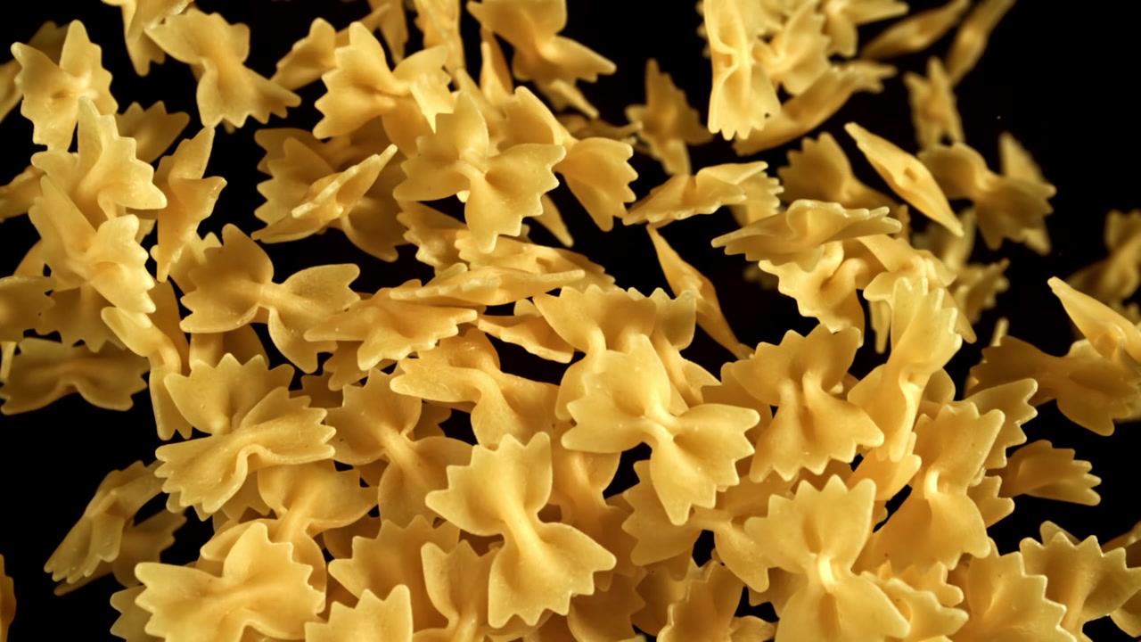 Pasta farfalle secca che cade al rallentatore su sfondo nero.