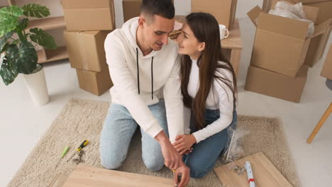 vista superior de una pareja joven en una casa nueva sentada en la alfombra montando un mueble