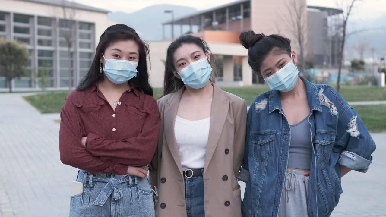 Portrait of a group of Asian female friends using a face mask while standing outdoors. New normal lifestyle concept.