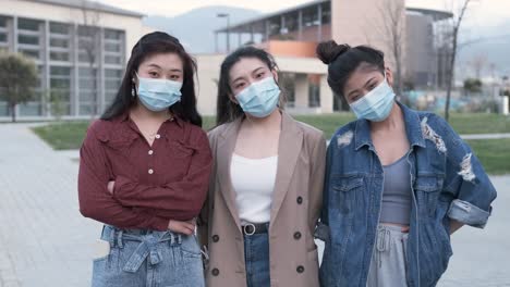 portrait of a group of asian female friends using a face mask while standing outdoors. new normal lifestyle concept.