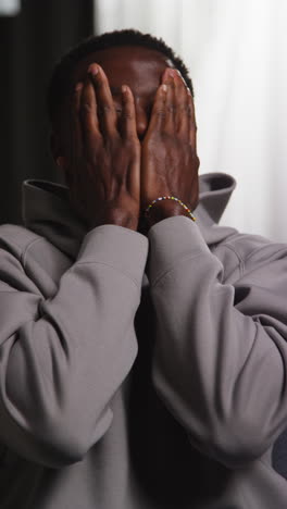 vertical video of unhappy and depressed young man sitting on sofa at home looking anxious and worried closing eyes and shaking head 2