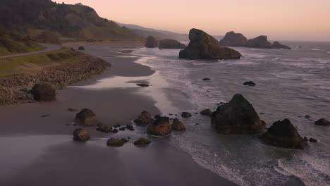 Drone-slowly-flying-backwards,-showing-sea-stacks-at-Myers-Creek-near-Pistol-River,-Southern-Oregon,-USA,-during-beautiful-sunset