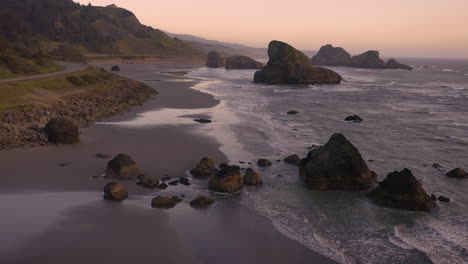 drone slowly flying backwards, showing sea stacks at myers creek near pistol river, southern oregon, usa, during beautiful sunset