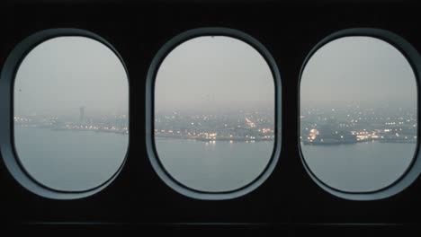 a serene view captured through porthole windows, showcasing a cityscape illuminated by distant lights amidst a misty atmosphere at twilight