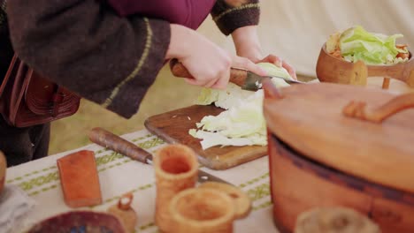 mujer con traje medieval cortando el repollo para preparar un plato histórico como siglos antes