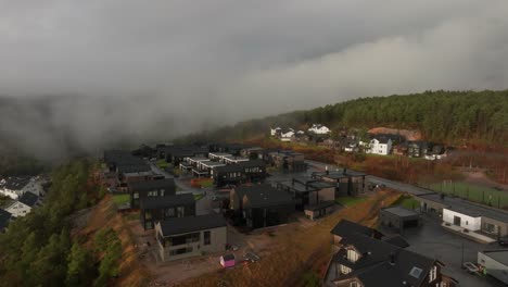 Drone-footage-of-housing-estate-in-Norway-with-some-fog-floating-in-th-air-and-sun-lighting-up-the-clouds