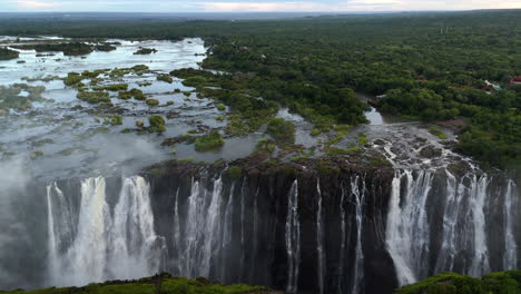 Aerial view of Victoria Falls with powerful waterfall plunging into gorge, mist rising above lush green forest, dramatic natural wonder and iconic travel destination in Africa