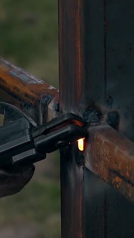 close view professional repairman in protective gloves welds metal rail to fence pole in house garden