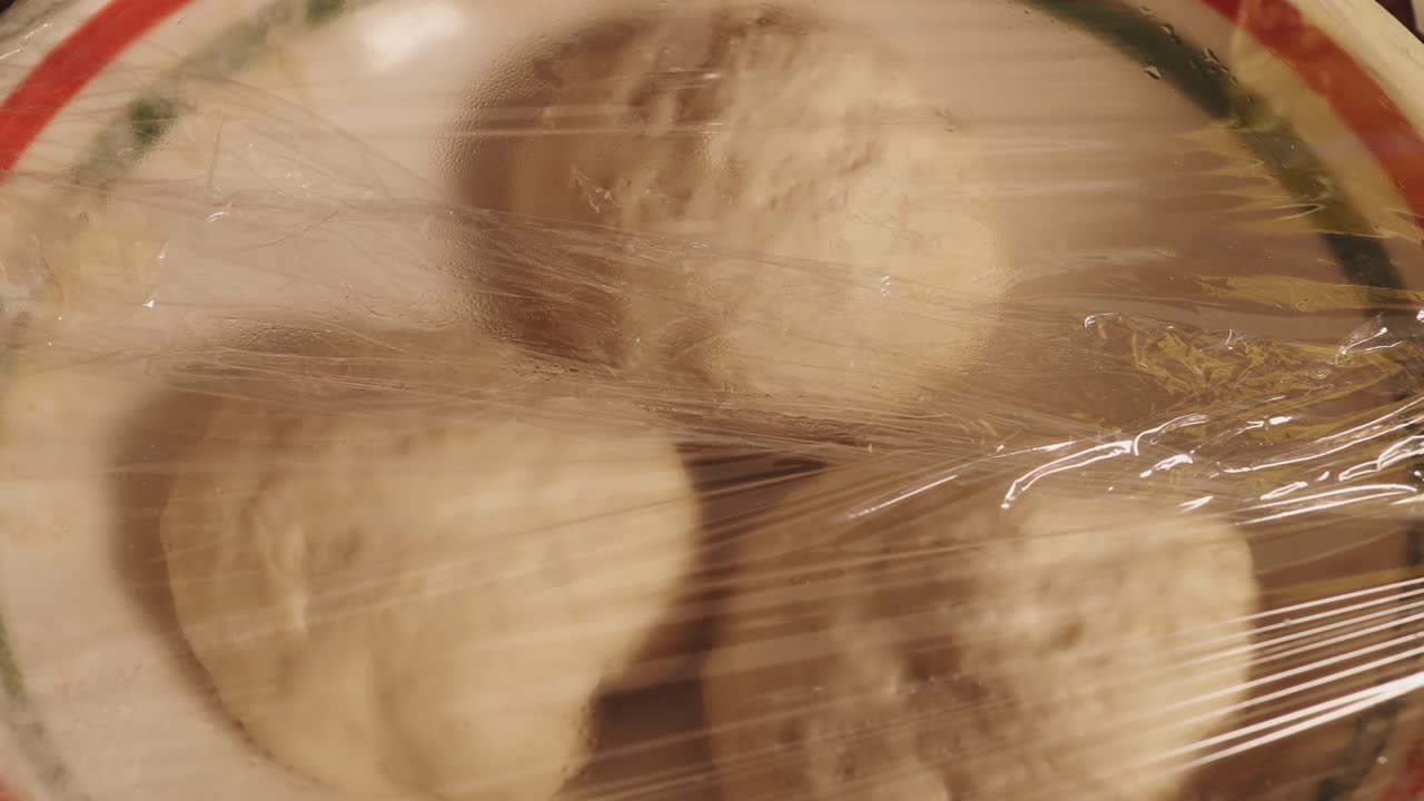 플라스틱 랩으로 덮인 접시 위에 반죽 세 조각 - 타임랩스