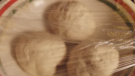 Three-Pieces-Of-Dough-On-A-Plate-Rising,-Covered-With-Plastic-Wrap---timelapse