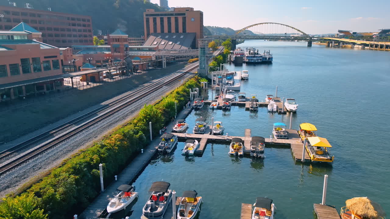 Small motor boats stand at the wooden berths in Pittsburgh, Pennsylvania. Railways go along the waterfront of the Allegheny River. Aerial view