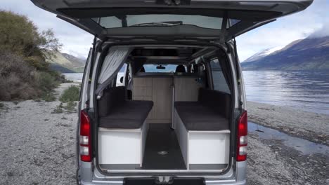 slowmo - exterior and interior of motorhome by beautiful blue lake wakatipu, queenstown, new zealand with mountains fresh snow cloudy sky in background