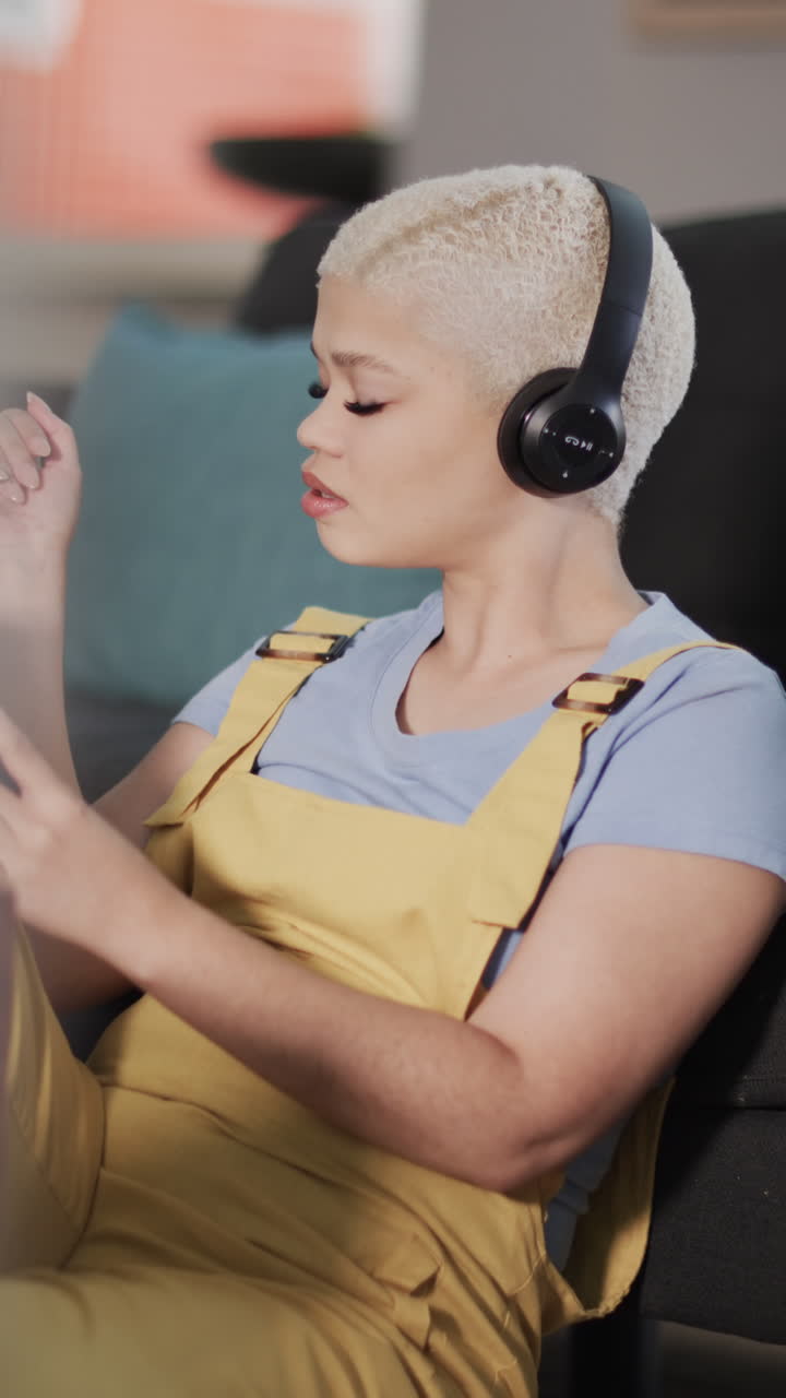 Vertical video of happy biracial woman listening to music at home in slow motion