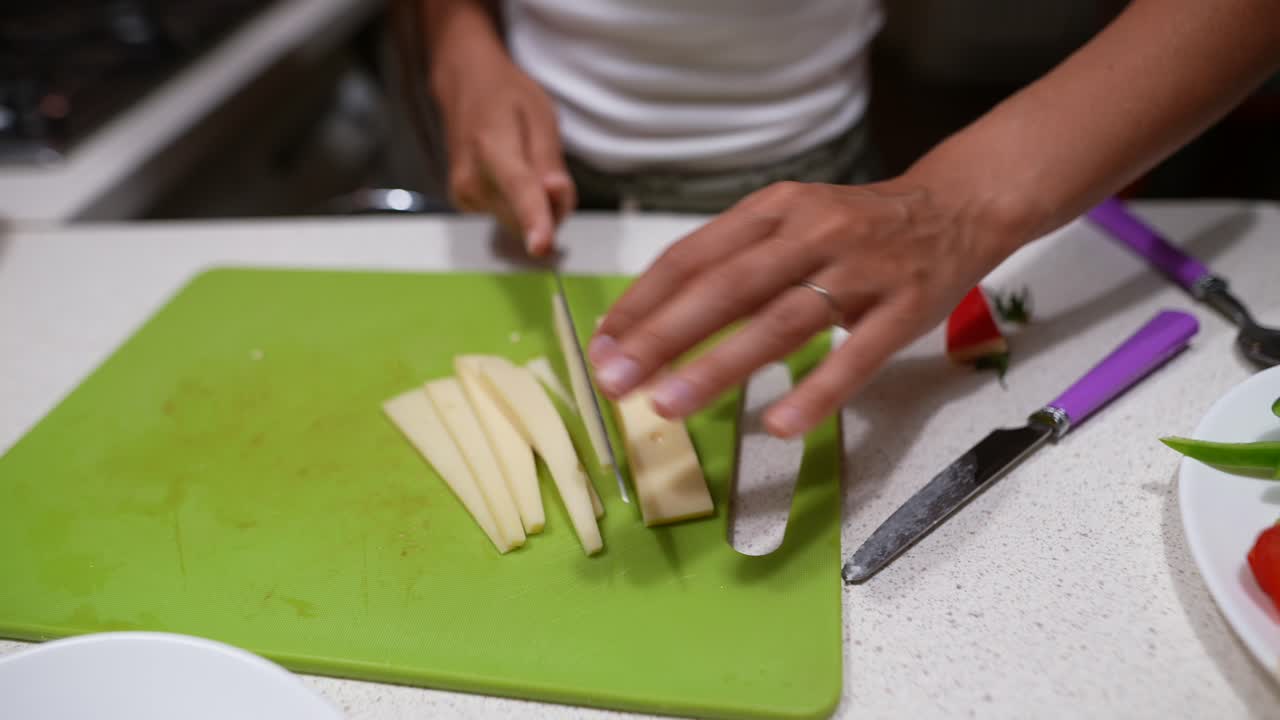 mujer cortando queso en una tabla de corte verde en la cocina