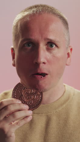 hombre conmocionado come galletas de chocolate con signos de bitcoin mirando a la cámara. hombre adulto se siente molesto debido al fallo de la criptomoneda en primer plano