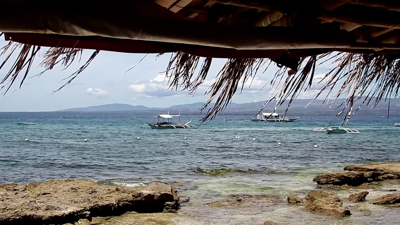 Tropical summer view of outrigger boats or bangka moored in the coast of Apo Island in Dauin Philippines seen from a hut roof, a famous travel destination
