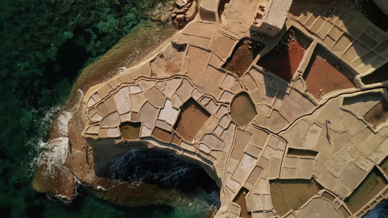 toma aérea de ángulo alto de un hombre que camina a través de charcos de salinas en xwejni durante una hermosa puesta de sol