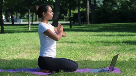 mujer meditando al aire libre con una computadora portátil