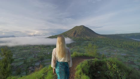 woman standing at kayupadi viewpoint enjoying view of mount batur, golden hour sunlight