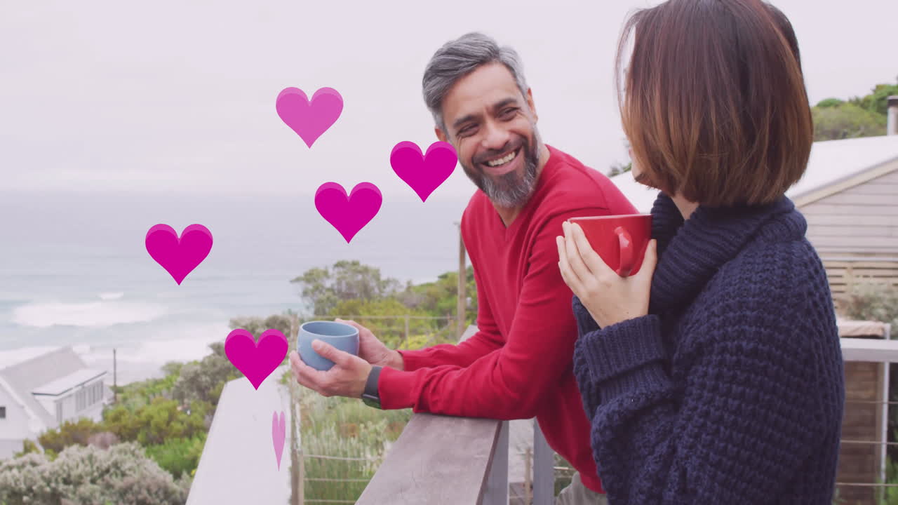 Animation of hearts over diverse couple drinking coffe on balcony