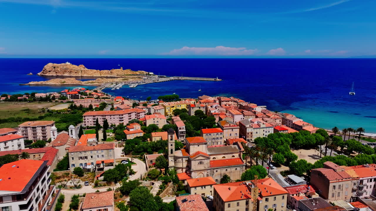 Aerial drone shot over the coastal town Île-Rousse in the Balagne region in Corsica, France. View of the beach and turquoise sea in the distance. Summer holidays destination