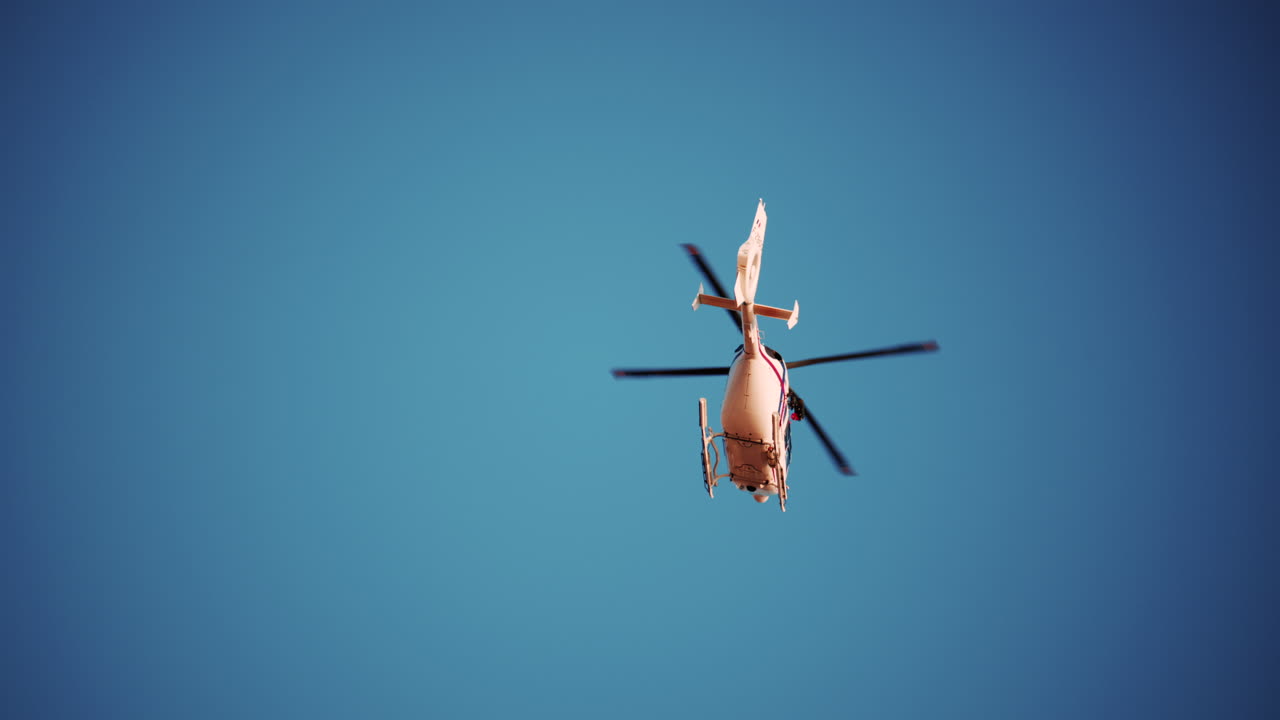 View of a white helicopter flying across a blue sky framed by blurred palm trees
