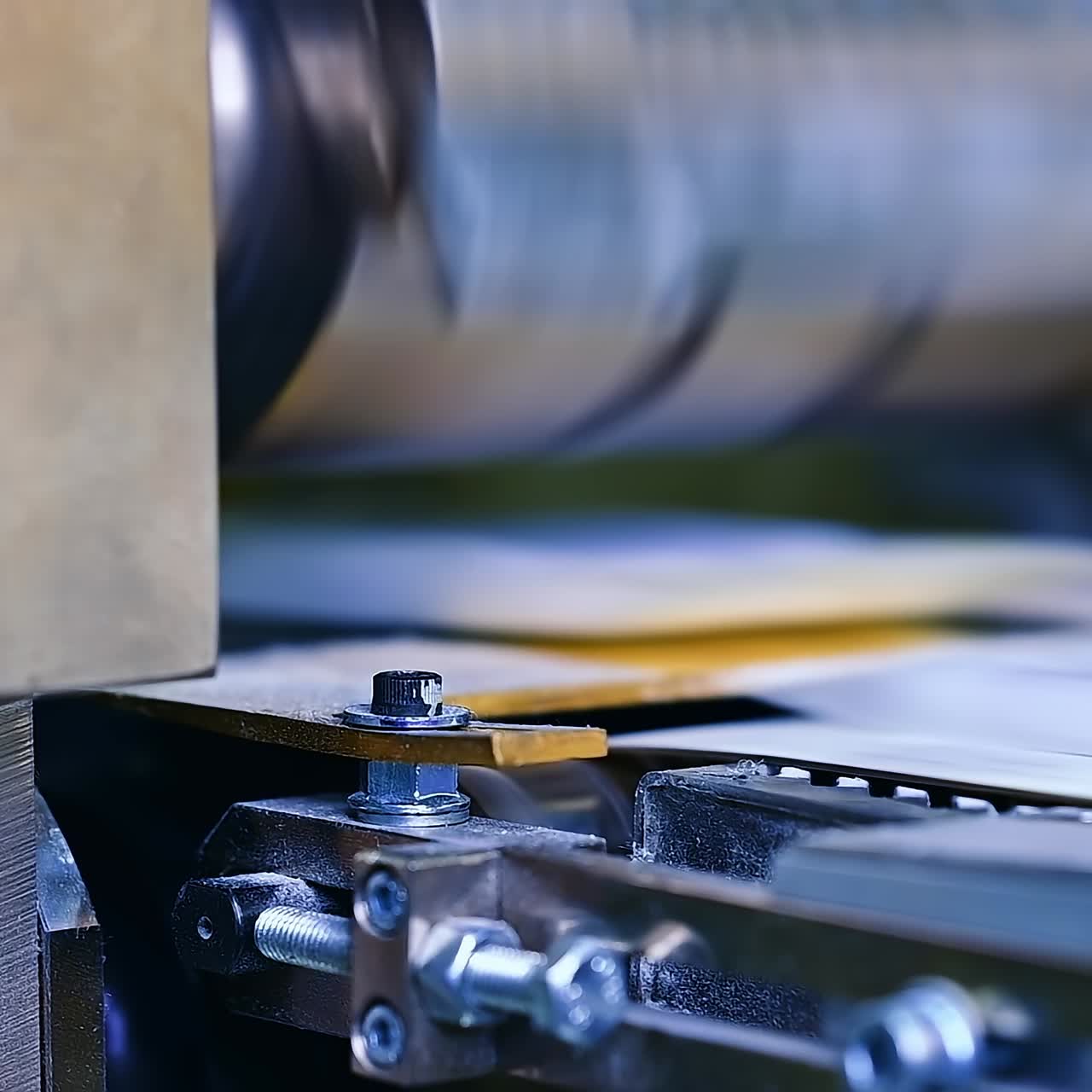 Strong bolts and internal screws holding a construction of a machine for producing diapers. A large rotating horizontal shaft over the conveyer belt blurred at the backdrop
