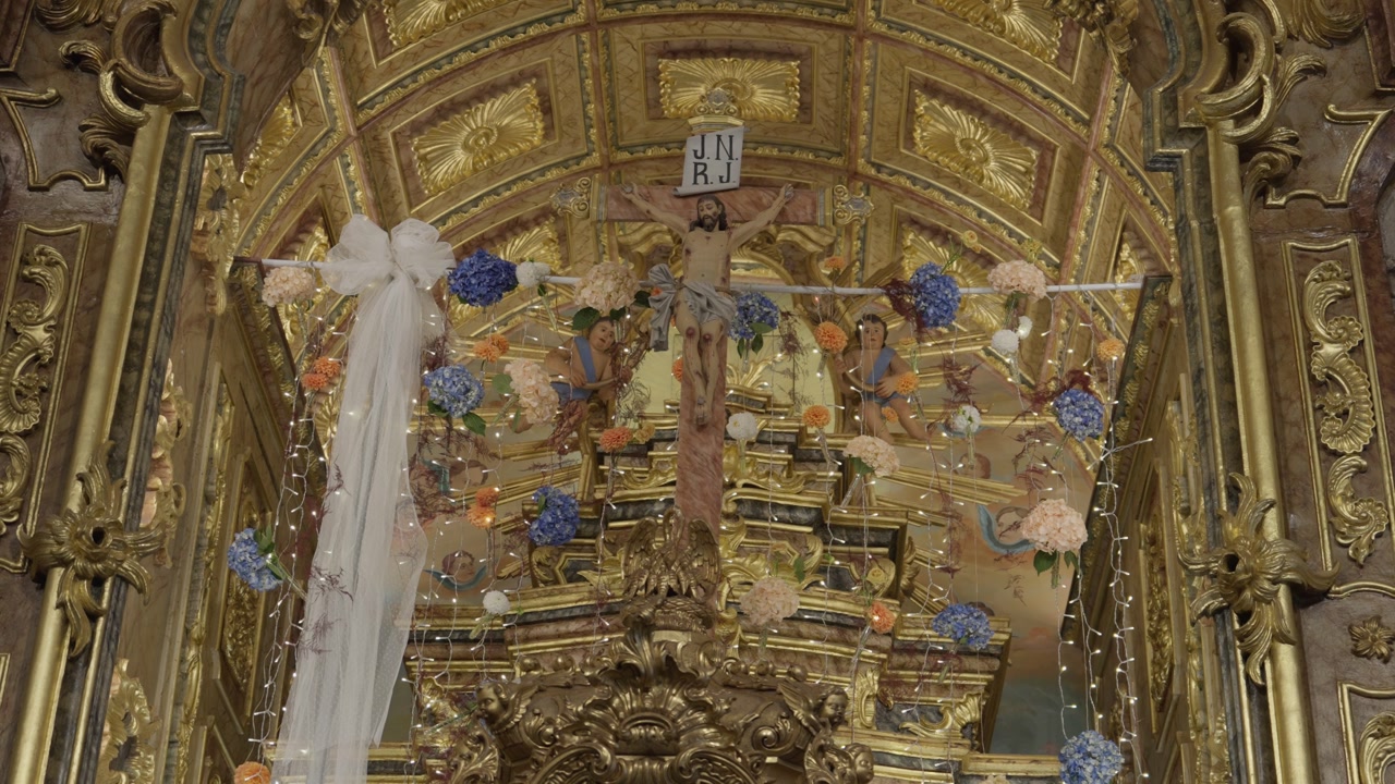 Close-up of a baroque altar featuring a wooden crucifix, intricate gold carvings, and fresh flower arrangements.
