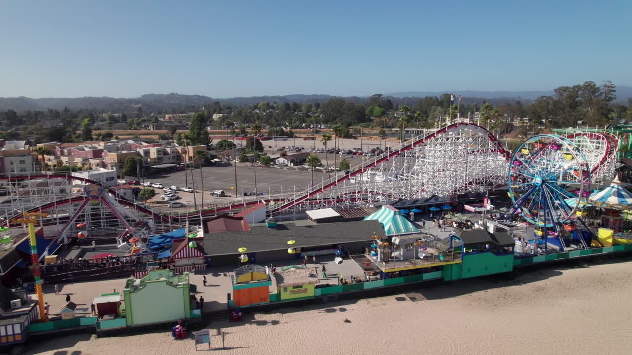 Long beachfront clip of boardwalk amusement park. Vintage-looking roller coasters, ferris wheels and merry-go-rounds. Santa Cruz Beach Boardwalk, California. 4K