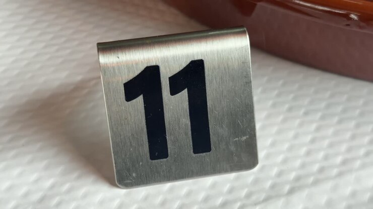 Primo piano di un cartello metallico con il numero 11 su un tavolo, con messa a fuoco sul simbolo numerico e sull'identificazione.