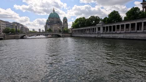 a moving camera glides over the spree river toward berlin cathedral on a bright day, capturing historic architecture, rippling water, and dynamic clouds