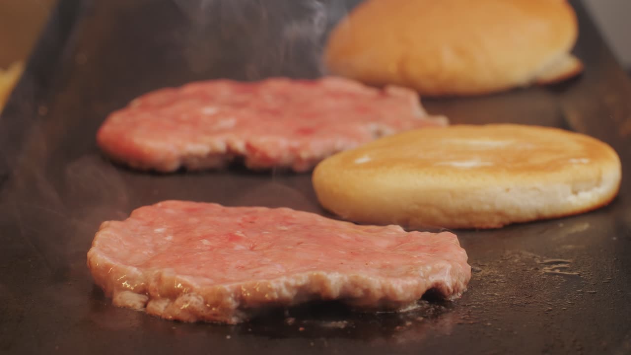 Cooking American fat smash burger on grill close-up. Beef or pork cutlet smashing by burger press. The chef in kitchen of the restaurant making cutlets for burgers - smash burger beefsteak. Fast and street food concept. High quality 4k footage