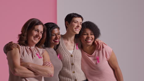 Studio-Portrait-Of-Multi-Racial-Group-Of-Women-Of-Different-Ages-Wearing-Pink-Breast-Cancer-Awareness-Ribbons-Hugging-Against-Pink-Background