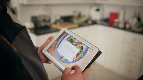 persona usando una tableta en una cocina, navegando por recetas de comida